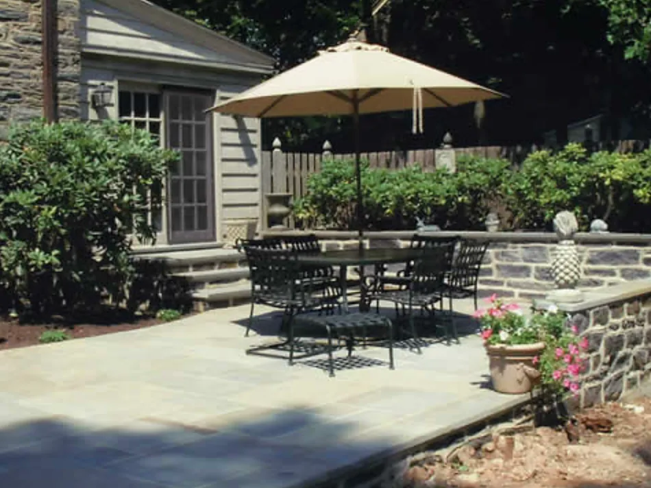 Bluestone terrace with a fieldstone seat wall beside a stone house